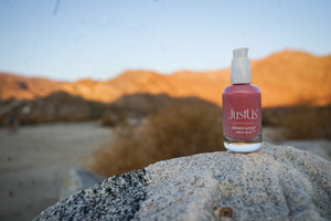 Pink Promise Justus skincare product on a rock with desert landscape in the background